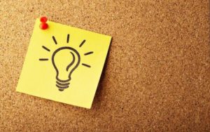 Yellow stickynote with lightbulb pinned to cork board.